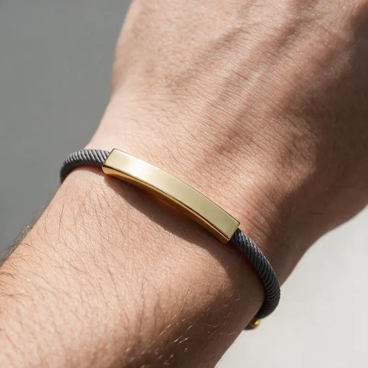 Voyager adjustable cord bracelet with gold ID bar, worn on a man's wrist.