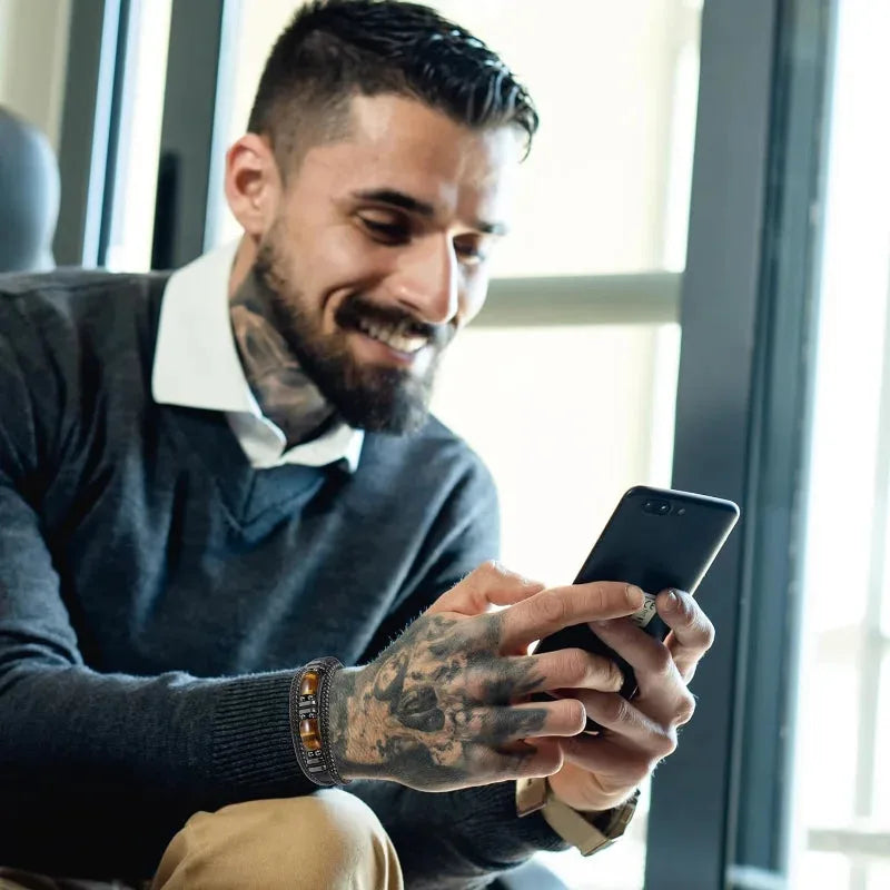 Man wearing a black leather tiger eye bracelet while using his phone