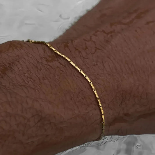 Gold wire chain bracelet worn on a wet wrist, with a reflective wet surface in the background.