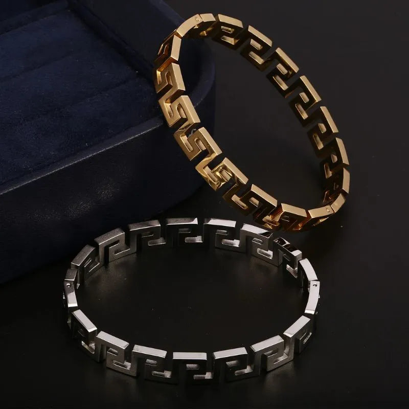 Gold and silver Greek key bangle bracelets displayed together beside a navy blue jewellery box on a black background
