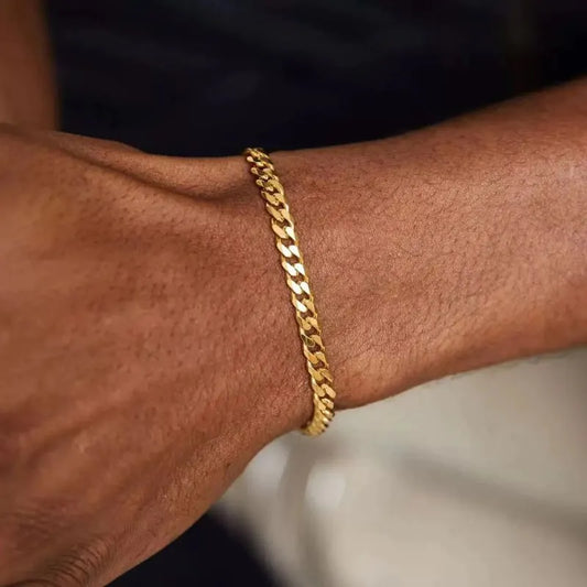 Close-up of a gold Cuban link bracelet resting on the wrist against a dark, blurred background.