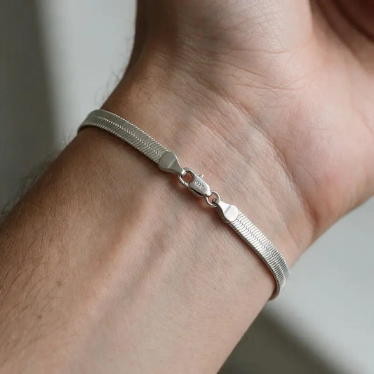 Silver flat blade chain bracelet with a '925' stamped clasp, worn on a man's wrist.