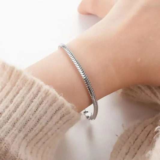 Close-up of the silver snake chain bracelet worn on the wrist, paired with a cream knit sweater sleeve.