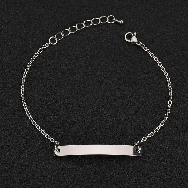 Silver thin chain bracelet with a plain rectangular nameplate and extension chain, on a black textured background.