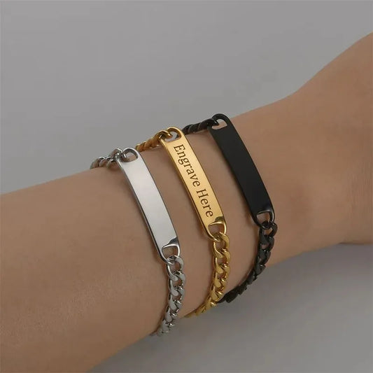 Silver, gold and black nameplate bracelets stacked on the wrist, the gold plate engraved with a sample message