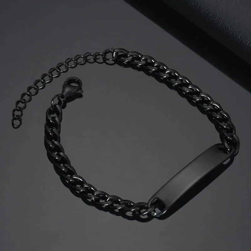 Blank black nameplate bracelet with a curb chain, resting on a dark leather surface