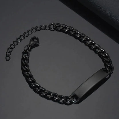 Blank black nameplate bracelet with a curb chain, resting on a dark leather surface