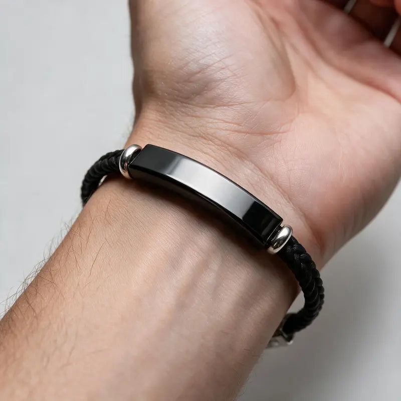 Renegade black braided cord bracelet with black ID plate, worn on a man's wrist.