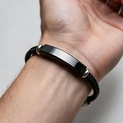 Renegade black braided cord bracelet with black ID plate, worn on a man's wrist.