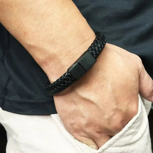 Black braided leather bracelet worn on the wrist, paired with a black t-shirt and cream pants.