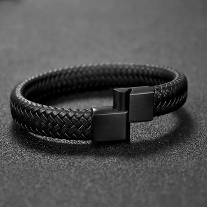 Black braided leather bracelet shown open and unclasped, laid in an oval on a dark grey textured surface.