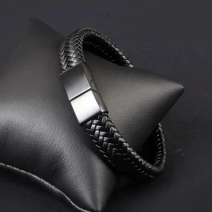 Black braided leather bracelet draped over a black leather display stand, clasp closed.