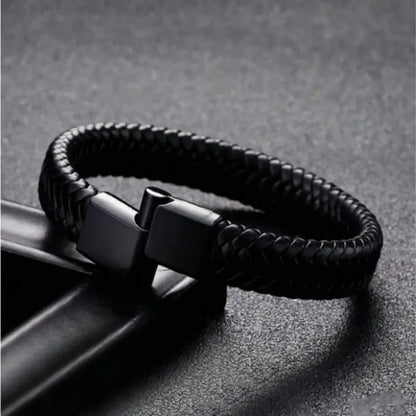 Black braided leather bracelet draped over an angular black leather stand, clasp shown open.