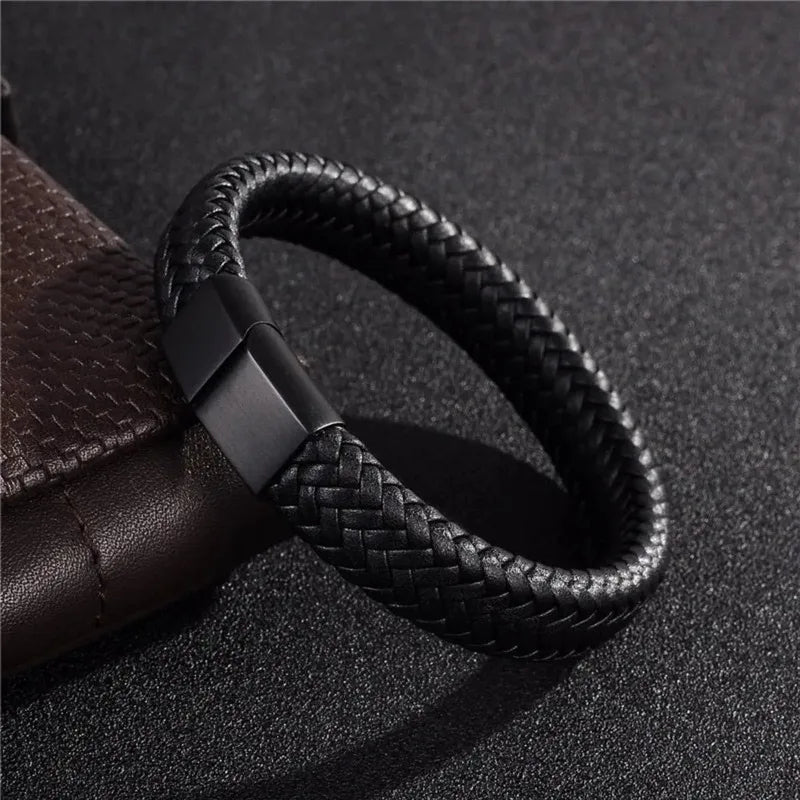 Black braided leather bracelet with a matte black magnetic clasp, laid on a dark textured surface next to a brown leather pouch.