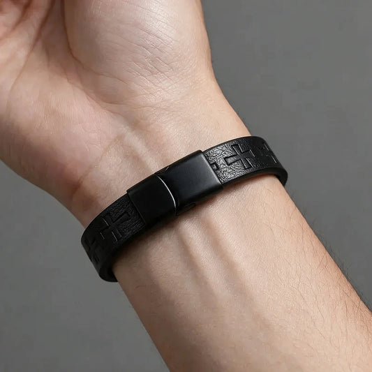 Black leather bracelet with an embossed repeating cross pattern and a matte black magnetic clasp, worn on a man's wrist.