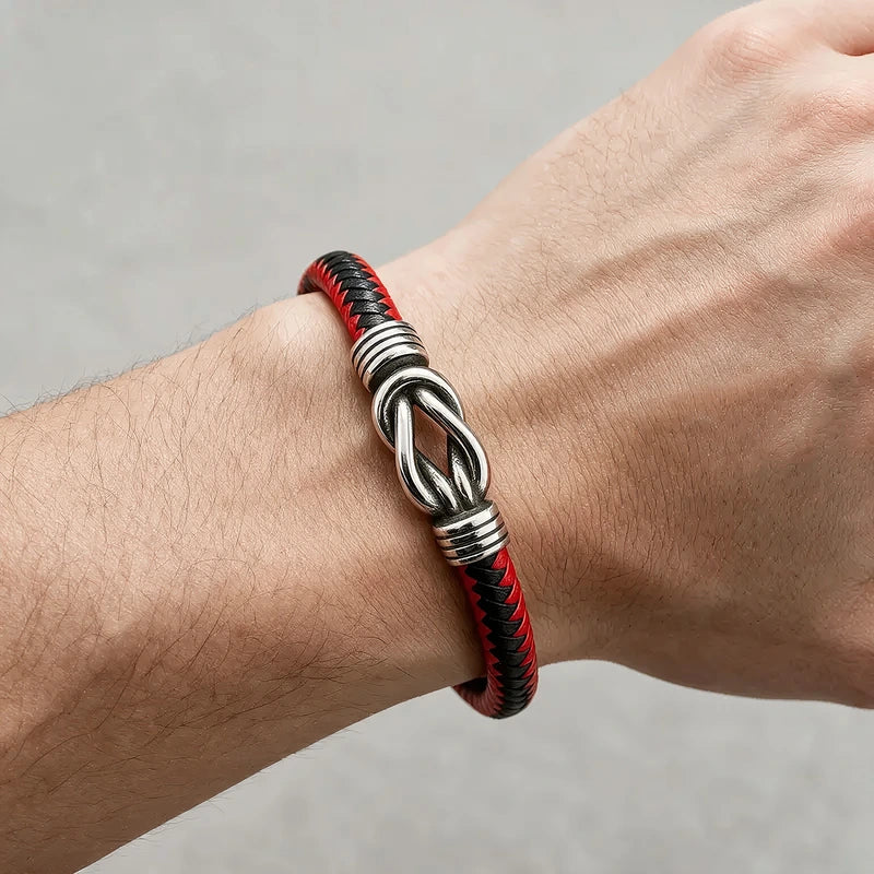 Black leather bracelet with a silver infinity-knot centerpiece clasp, worn on a man's wrist.