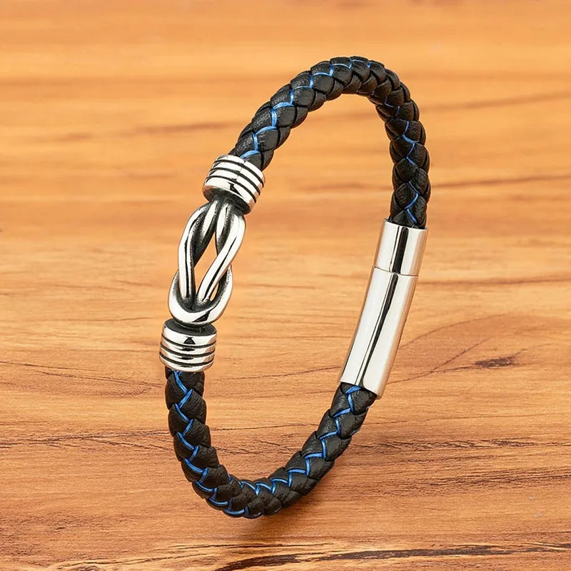 Black and blue braided leather bracelet with a polished stainless steel infinity-knot clasp, on a wood background