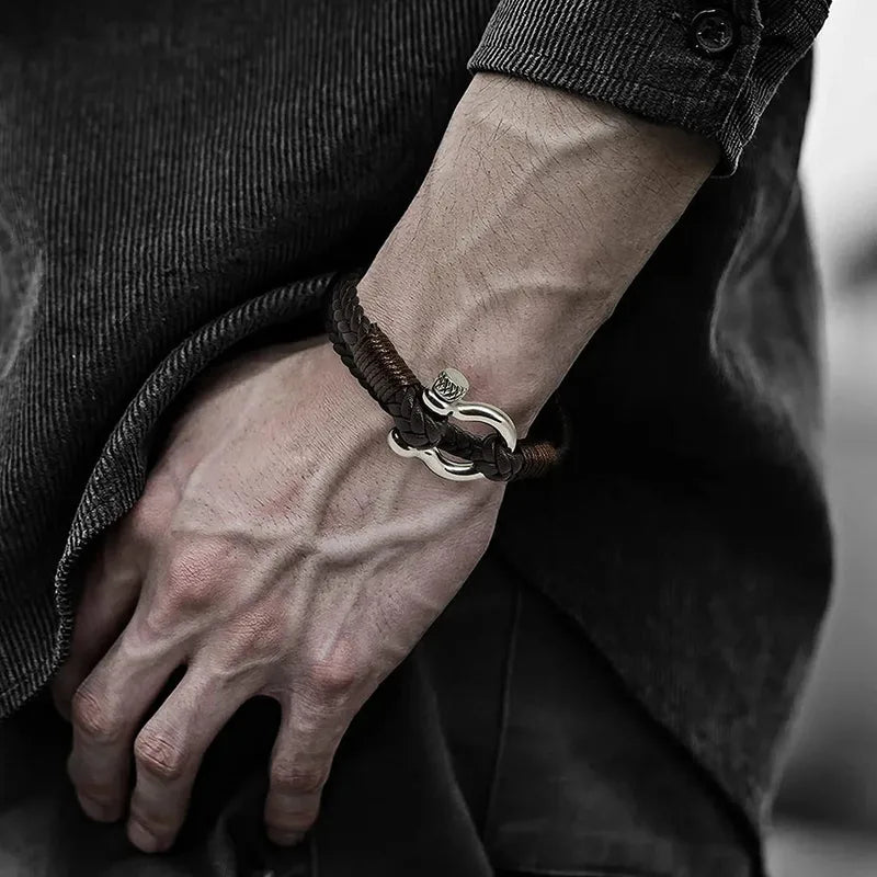 Close-up of a brown braided leather bracelet with a stainless steel shackle clasp worn on the wrist