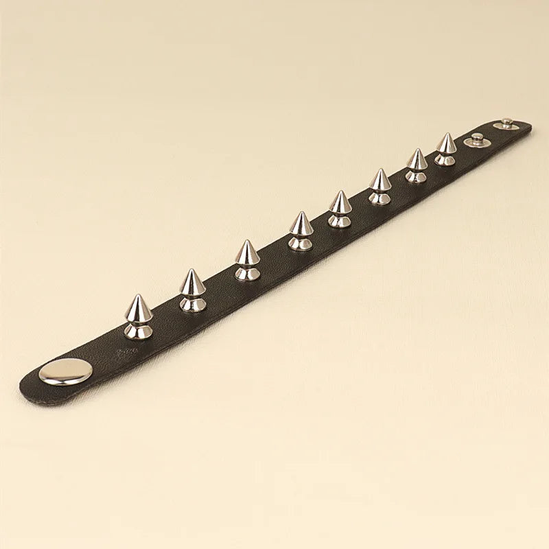 Black leather cuff bracelet with a single row of silver spike studs, on a cream background