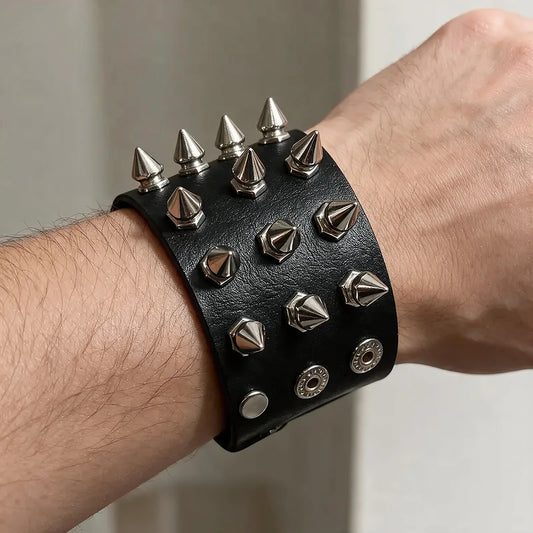 Black leather cuff bracelet with rows of silver cone-shaped spike studs, worn closed on a man's wrist.
