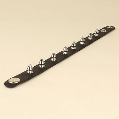 Black leather cuff bracelet with a single row of silver spike studs, on a cream background