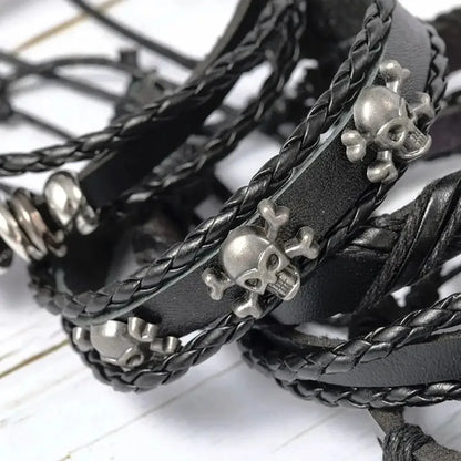 Close-up of silver skull-and-crossbones charms on braided black leather bracelet strands.