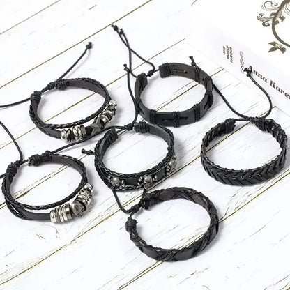 Six individual black leather bracelets from the Pentagon and Skull set laid out separately on a wooden surface with a book.