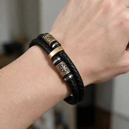 Black double-strand leather bracelet with an antique bronze Norse rune charm bead, worn on a man's wrist.