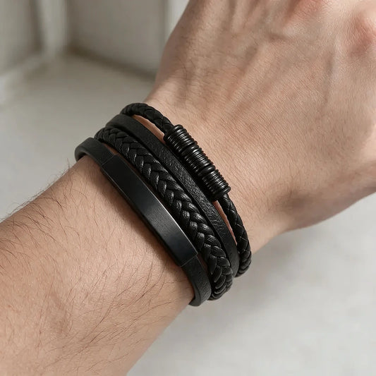 Multi-strand black leather bracelet with a brushed metal ID plate and a wrapped spacer bead, worn on a man's wrist.
