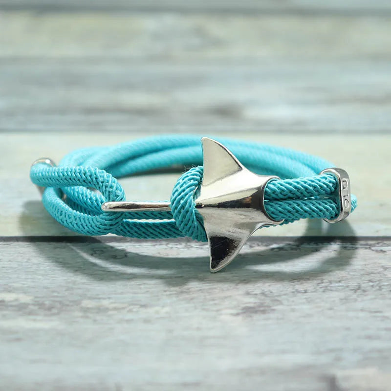 Manta ray charm in silver finish on a sky blue rope bracelet, resting on a wood surface