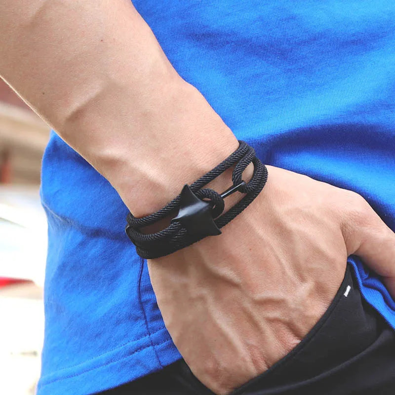 Whale tail charm in black finish on a black rope bracelet, worn on the wrist