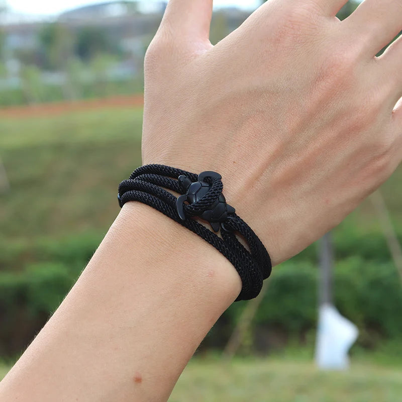 Sea turtle charm in black finish on a black rope bracelet, worn on the wrist outdoors