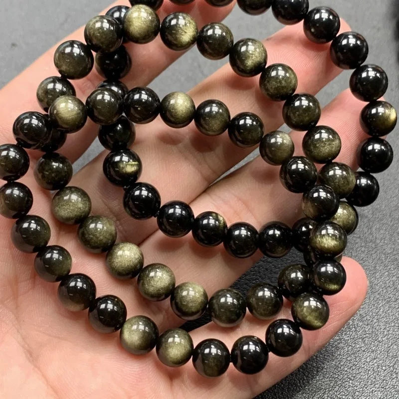 Golden obsidian bead bracelets held in hand, gold sheen detail