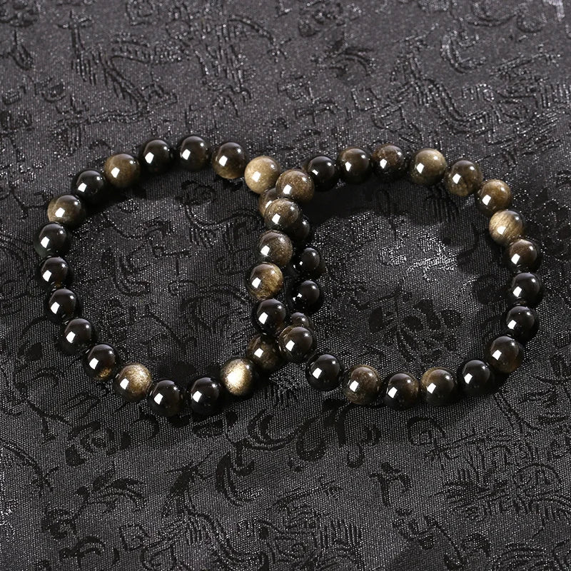Two golden obsidian bead bracelets laid together on patterned fabric
