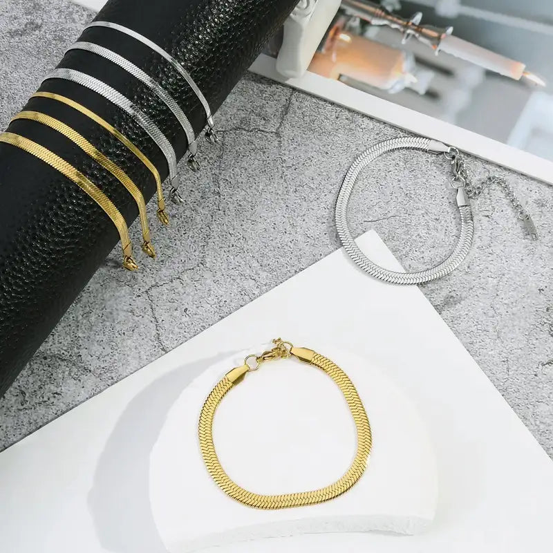Gold and silver flat herringbone chain bracelets in various widths, laid flat and on a display stand