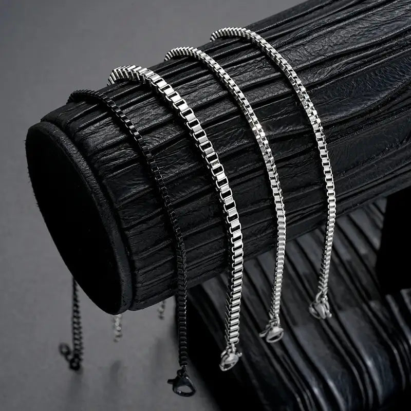 Four box chain bracelets in different widths draped over a leather display stand