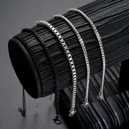 Four box chain bracelets in different widths draped over a leather display stand