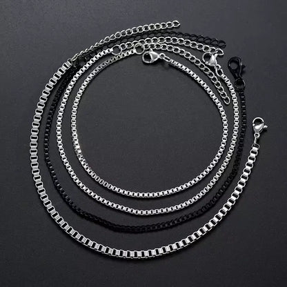 Four stainless steel box chain bracelets, three silver and one black, each with its own lobster clasp and extension chain, coiled together