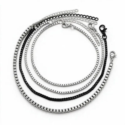 Set of four stainless steel box chain bracelets, three silver and one black, each with a lobster clasp and extension chain, product photo on white background