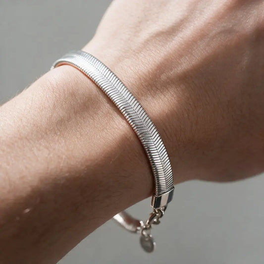 Wide flat silver herringbone chain bracelet worn on the wrist
