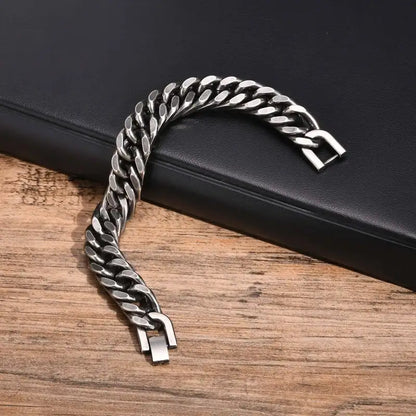 Close-up of the fold-over clasp mechanism on a gunmetal Cuban link bracelet, unclipped on a wood surface