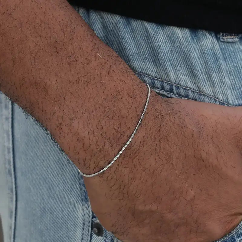 Silver snake chain bracelet worn on the wrist, paired with denim jeans