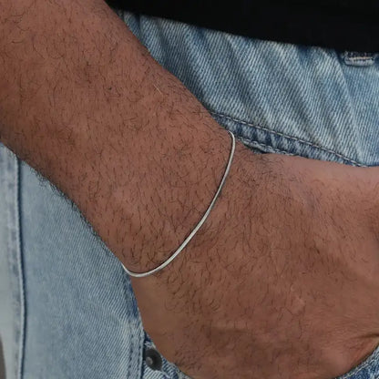 Silver snake chain bracelet worn on the wrist, paired with denim jeans