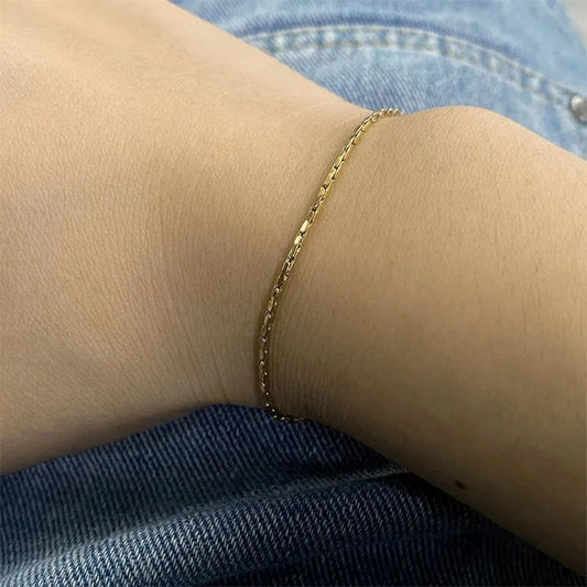 Gold hammered wire chain bracelet worn on the wrist, resting against denim jeans.