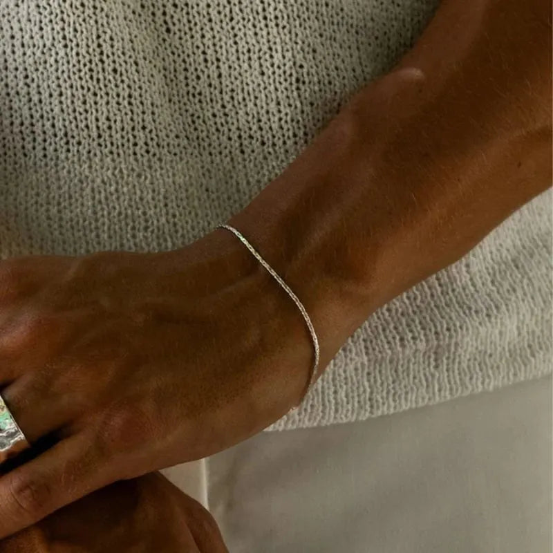 Silver-tone hammered wire chain bracelet worn on the wrist, resting near a knit sweater with a ring visible on the other hand.