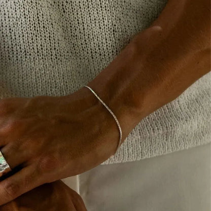 Silver-tone hammered wire chain bracelet worn on the wrist, resting near a knit sweater with a ring visible on the other hand.