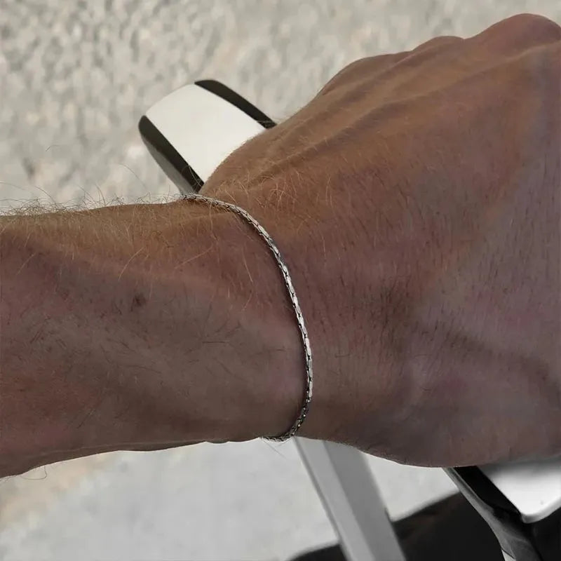 Silver-tone hammered wire chain bracelet worn on the wrist, resting on a stone ledge outdoors.