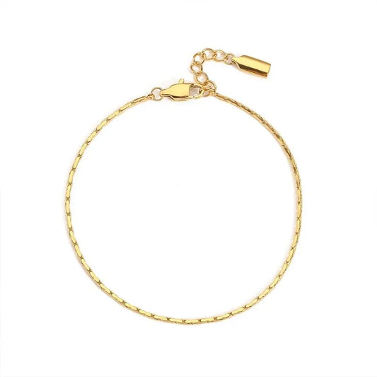 Gold hammered wire chain bracelet laid in a circle on a white background, with the lobster clasp and drop charm visible.