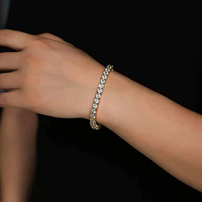 Gold tennis bracelet worn on the wrist, close-up against a black background.