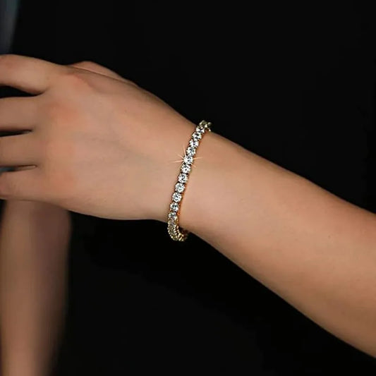 Gold tennis bracelet worn on the wrist, close-up against a black background.